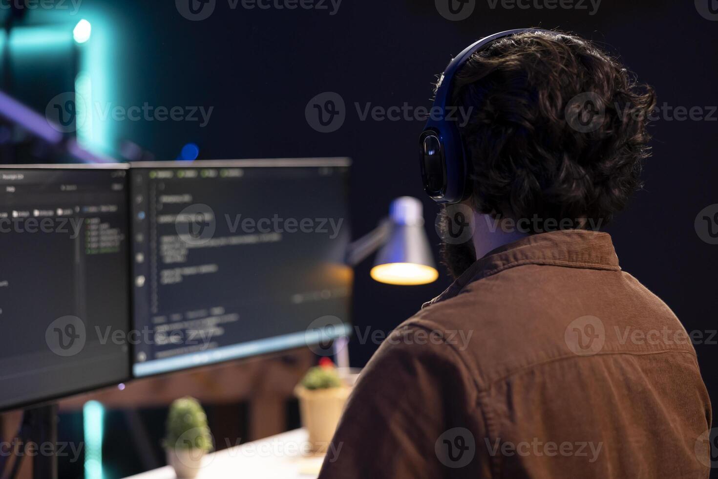 Cybersecurity specialist listening music while looking for company security vulnerabilities, preventing malware infections. Programmer with headphones on preventing cyber attacks on PC photo