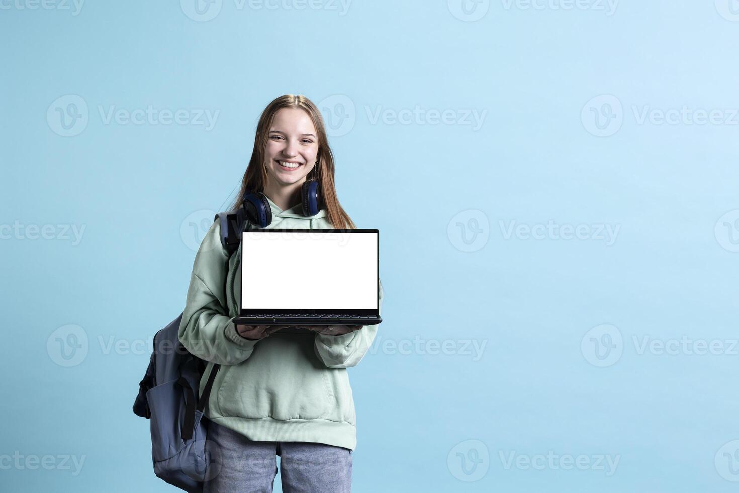 Jolly girl presenting laptop with isolated screen display, doing advertisement, smiling, studio background. Happy teenager creating ad promotion with mockup notebook device photo