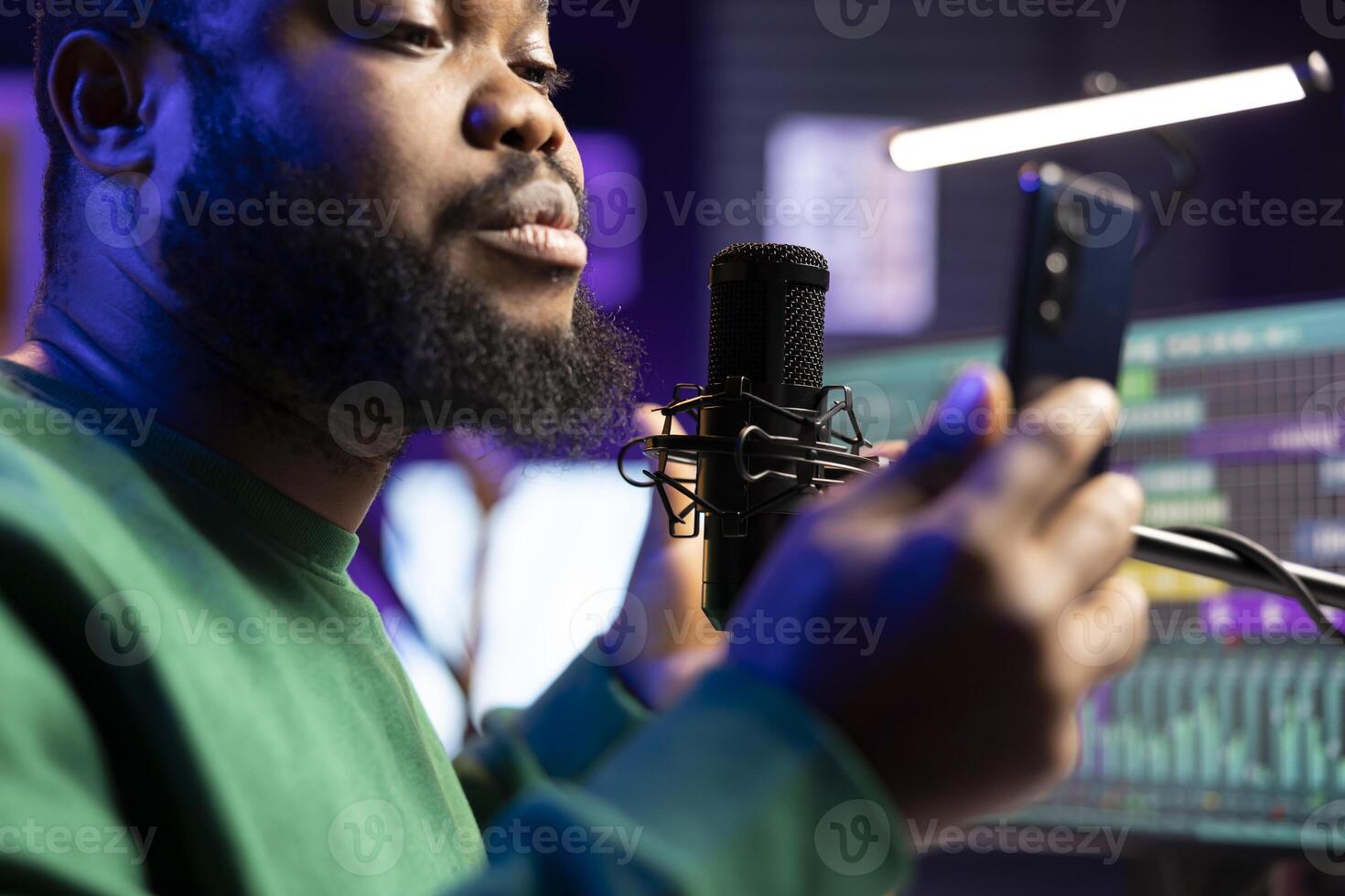 Young songwriter musician singing an acoustic version of his latest creation, live recording session on microphone in home studio. Artist producing new music, reading verses on his phone. Close up. photo