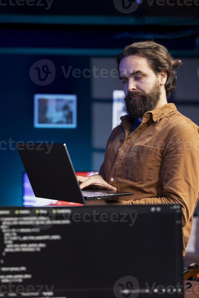 Computer scientist walking in apartment designing and developing software applications using laptop. IT professional standing in living room, implementing and maintaining company systems photo