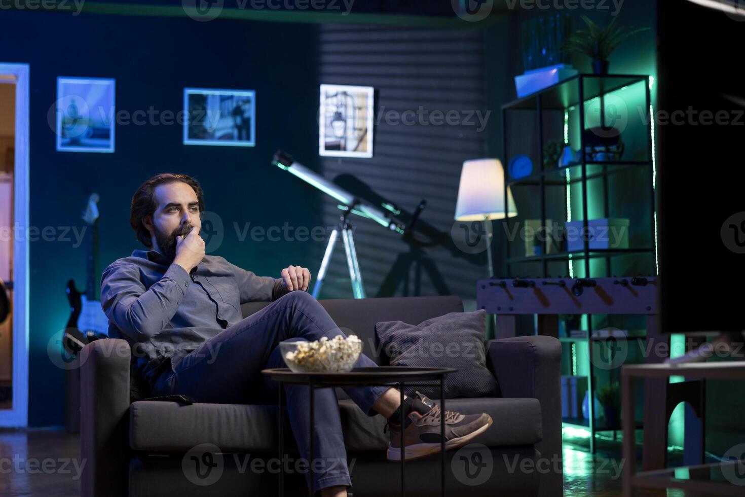 Cord cutter sitting on couch eating popcorn in front of TV displaying streamed movie. Upbeat person at home consuming snacks and watching on demand channels on television screen photo