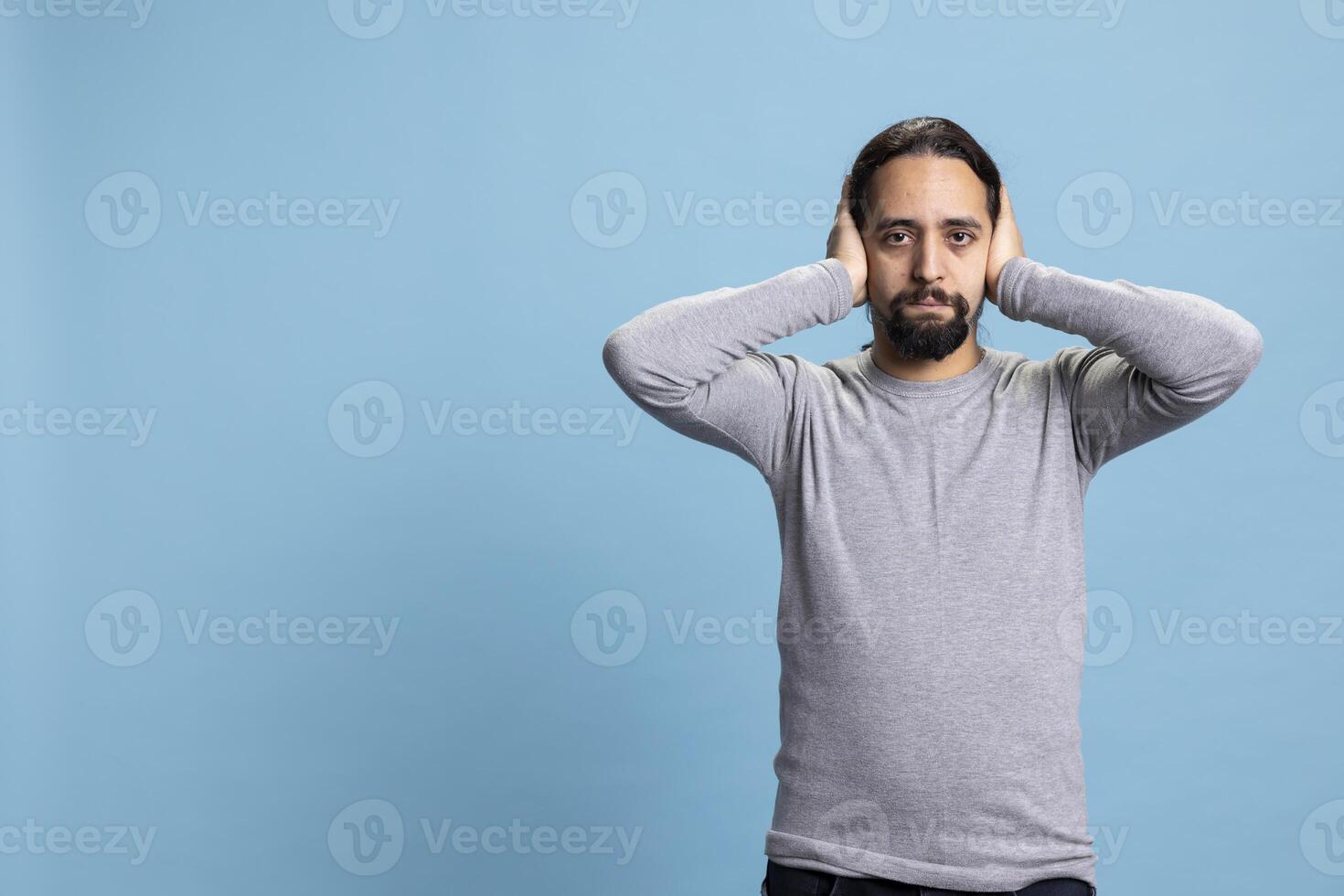 Middle eastern man covering his ears as part of the three wise monkeys illustration, showcasing the moral motivational idiom in studio. Young person hearing no evil with traditional wisdom metaphor. photo