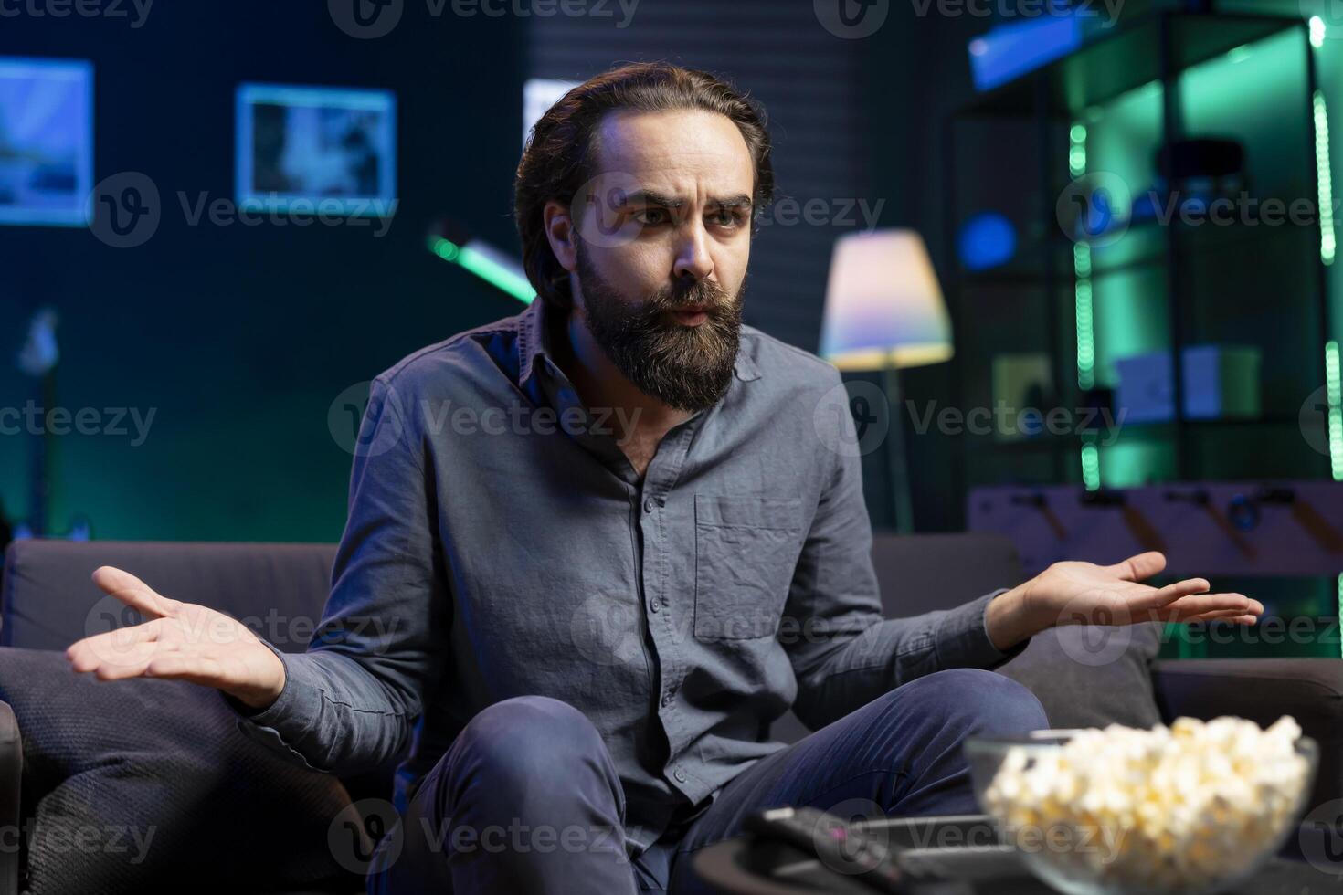 Puzzled person on couch using TV to binge thriller series on subscription based streaming services, disagreeing with characters. Man watching VOD shows on television display, feeling confused by plot photo