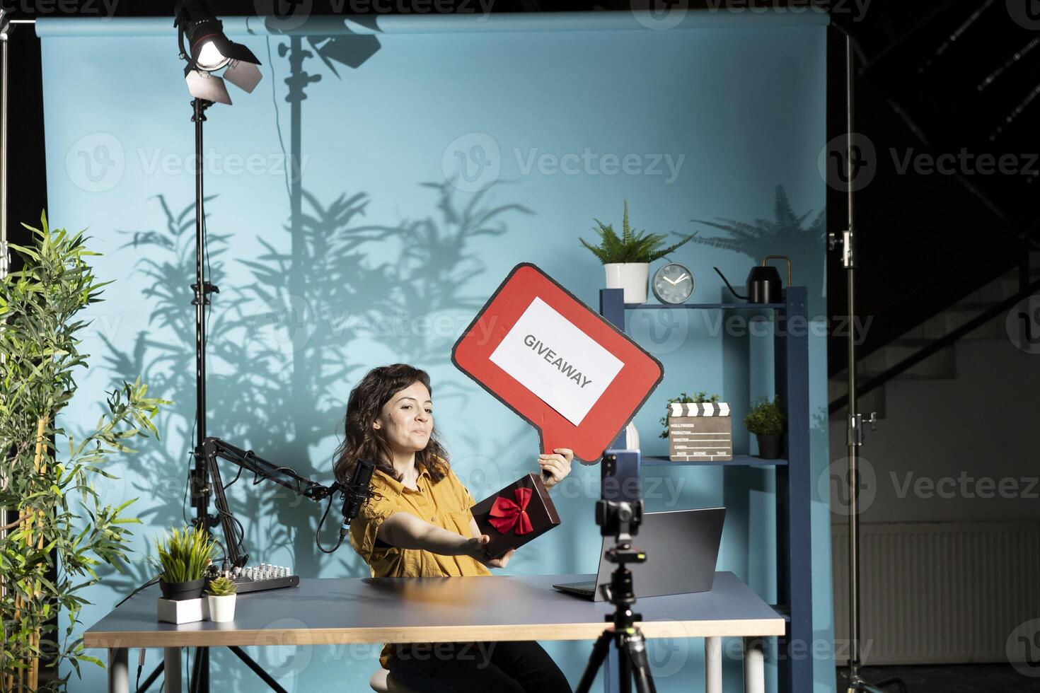 Social media influencer presenting giveaway for audience, holding gift box and cardboard sign, filming with specialized gear. Woman running contest, advertising it with copy space board photo