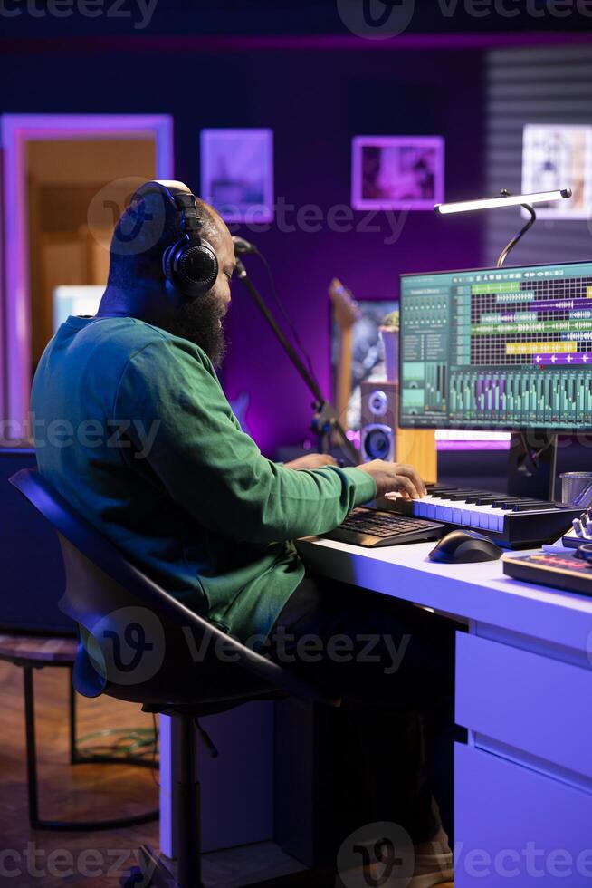 Music composer plays electronic keyboard piano keys and recording new tracks, creating audio recordings before launching music. Artist producer uses synthesizer and amplifier, post production. photo