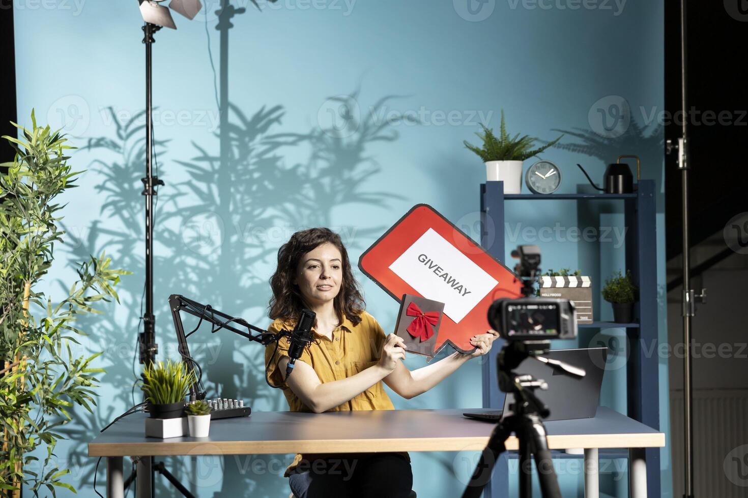 Social media influencer presenting giveaway for audience, holding gift box and cardboard sign. Content creator creating contest for her online community, filming with professional camera photo