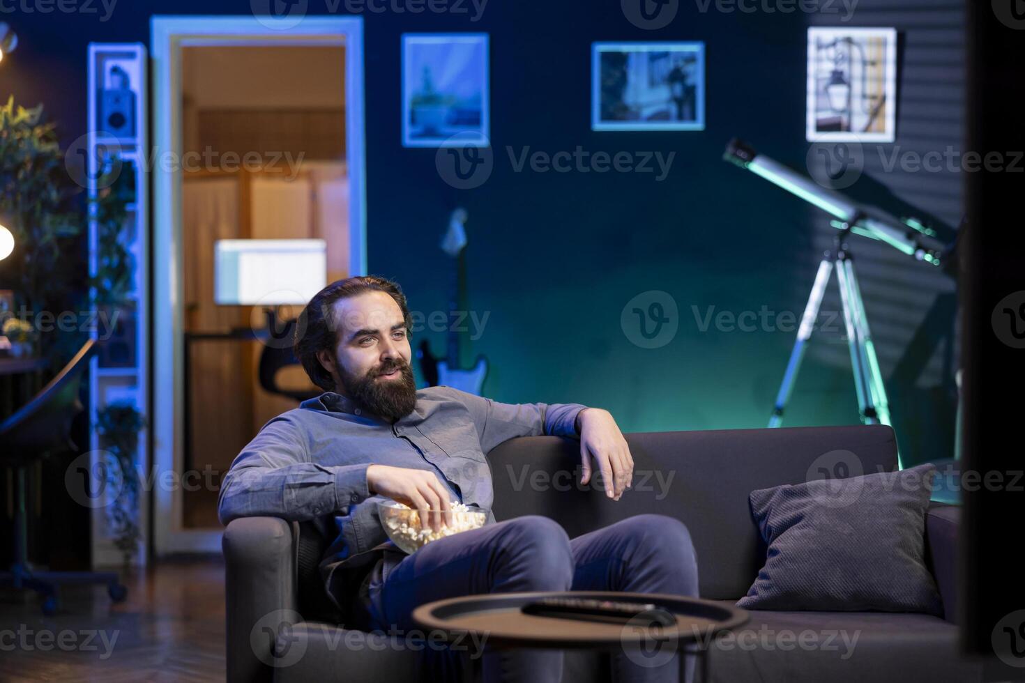 Smiling cord cutter sitting on couch in front of TV displaying streamed movie. Upbeat person at home watching television screen showing on demand channel with shows photo