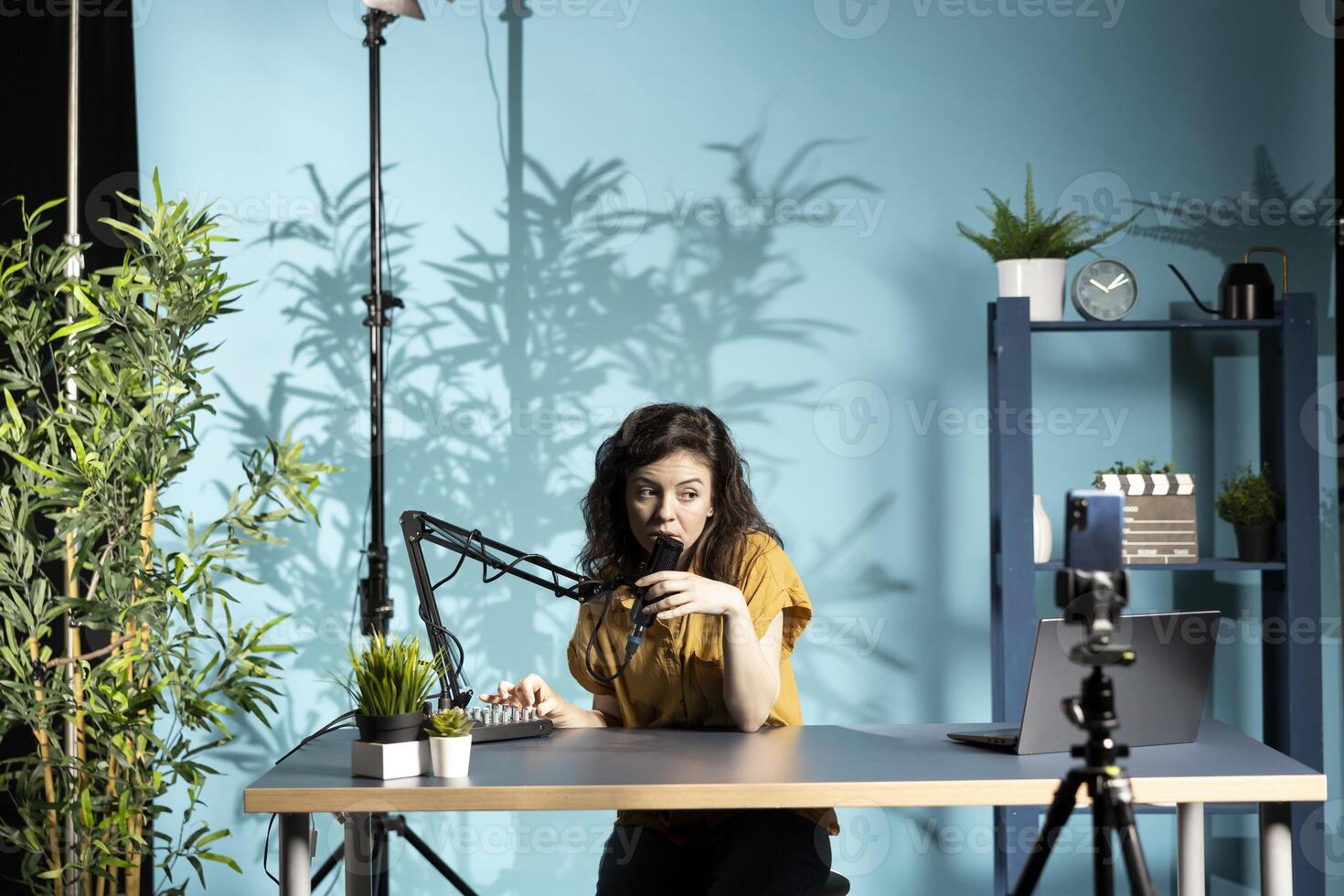 Content creator positioning professional microphone closer, ensuring it captures clear audio for upcoming , filming with smartphone on tripod. Vlogger checking audio levels, recording with phone photo