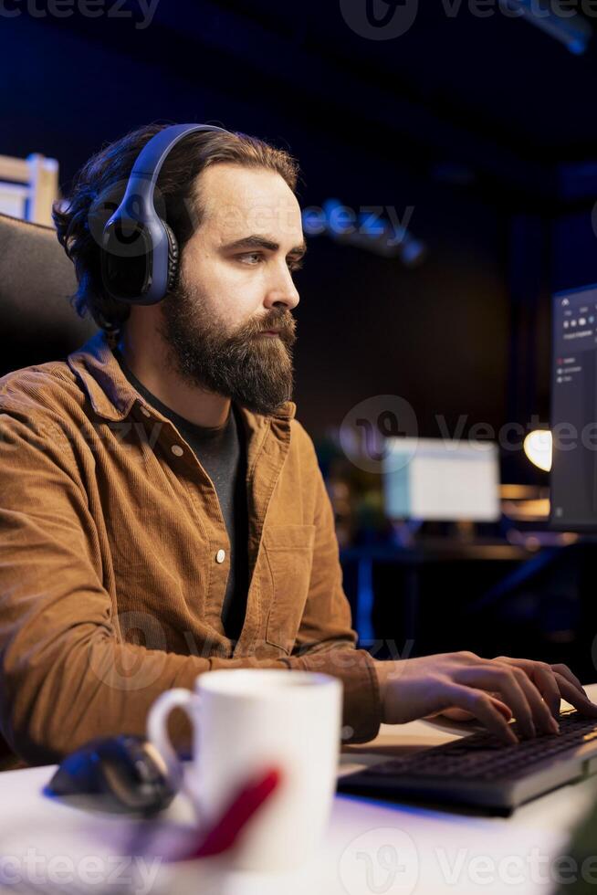 Cybersecurity specialist listening audiobooks on stereo headphones while looking for security vulnerabilities. Programmer enjoying podcasts while preventing PC cyber attacks photo