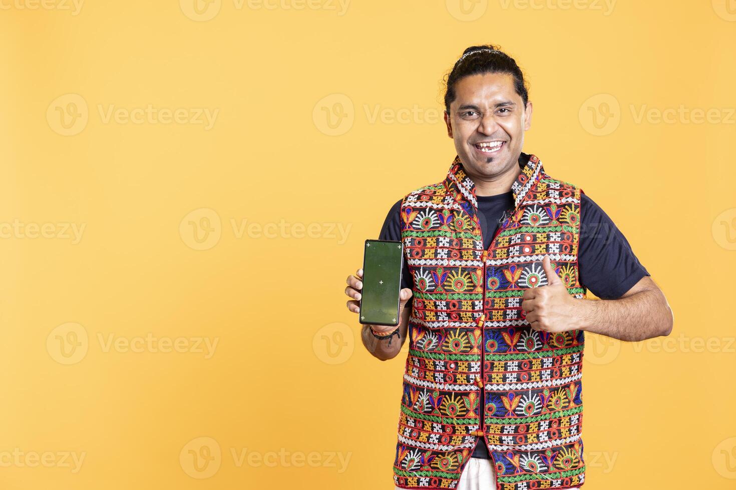 Portrait of joyous content creator doing thumbs up gesturing, recommending isolated screen phone, studio backdrop. Joyful man reviewing mockup smartphone, doing like sign gesturing photo