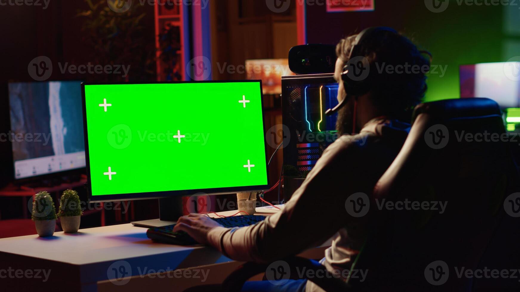 Man in dimly lit apartment playing games on green screen gaming PC at computer desk, enjoying day off from work. Gamer battling enemies in online multiplayer shooter on mockup monitor photo