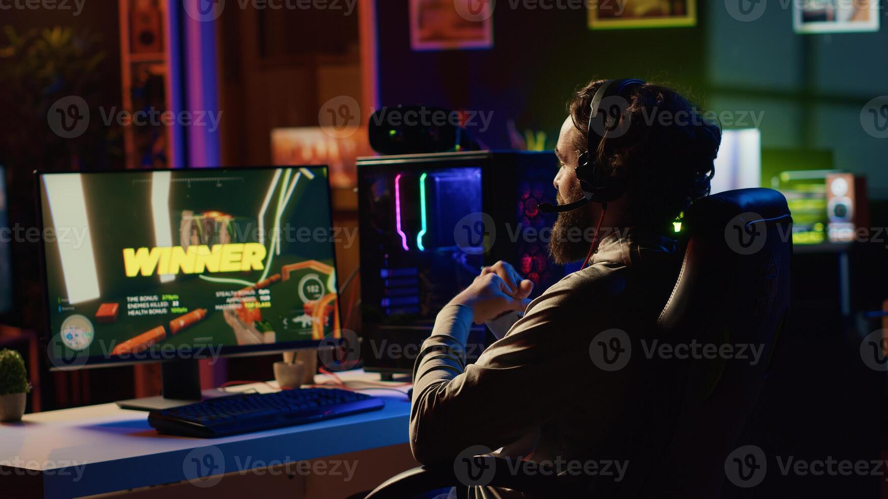 Man happy after finishing videogame, receiving winning message on gaming PC screen in dimly lit apartment. Gamer being victorious after battling enemies in singleplayer shooter photo