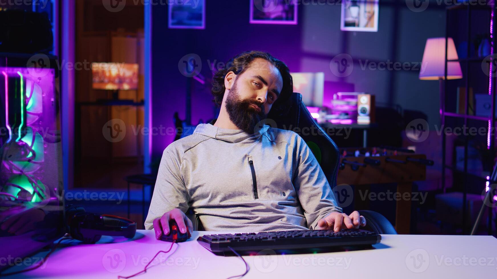 Drowsy man feeling tired after obsessively playing videogames all day, struggling to stay awake, unable to control addiction. Sedentary gamer falling asleep on chair while competing in online game photo