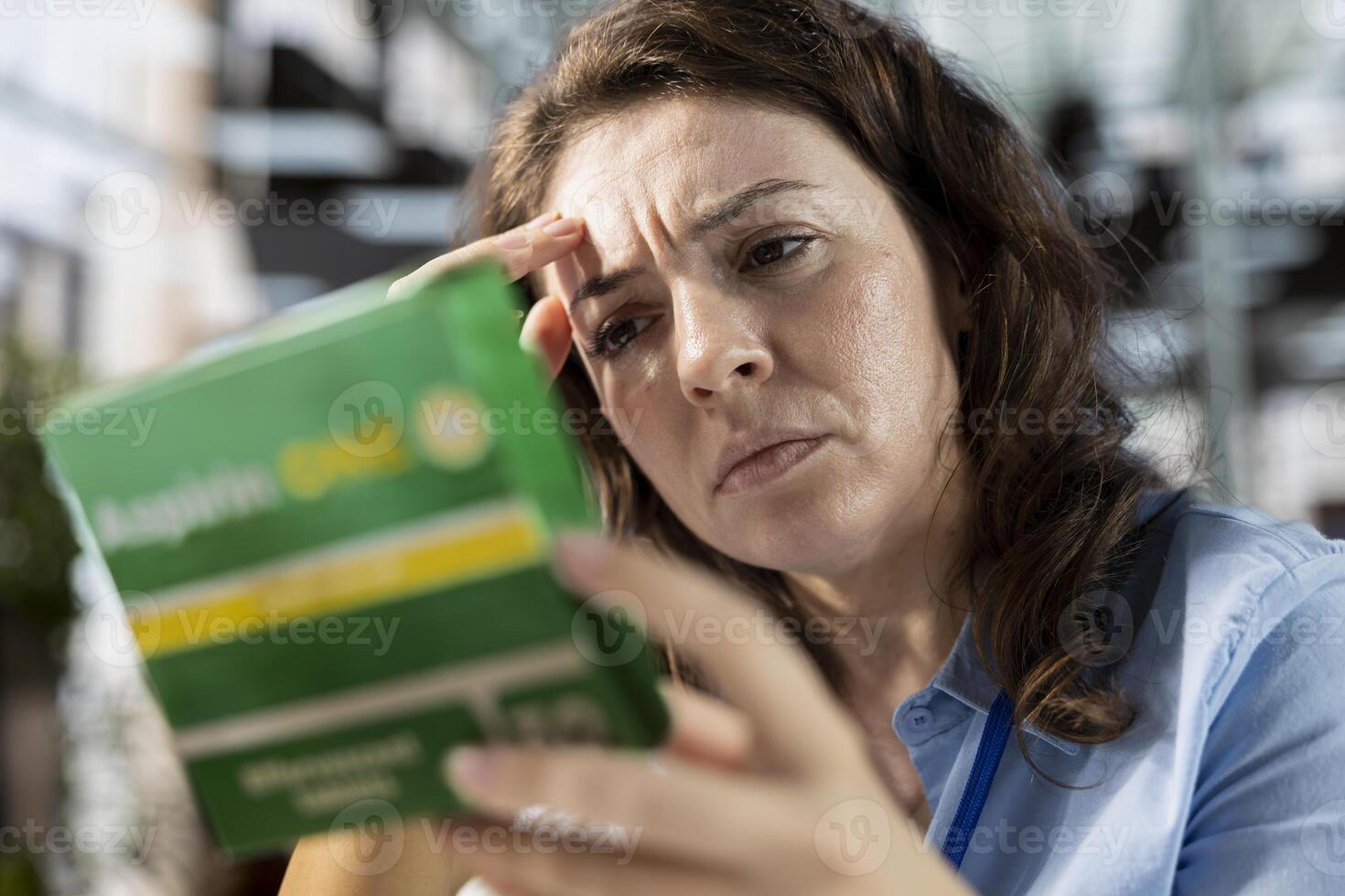 Businesswoman with a headache preparing to take a painkiller medicine in order to solve her daily organizational tasks, reading the recommended dosage on the box label. Aspirin pills. photo