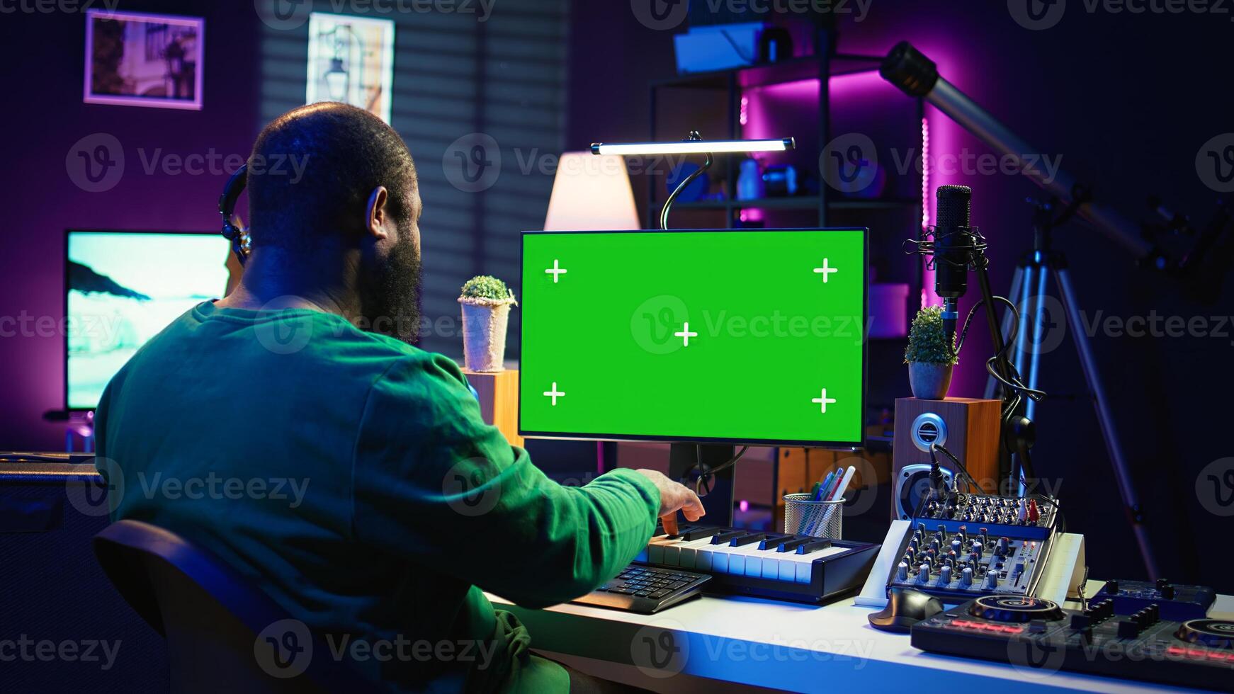 Artist plays midi controller synthesizer next to green screen layout, working on producing new music with his audio musical instruments in home studio. Musician using isolated copy space. Camera B. photo