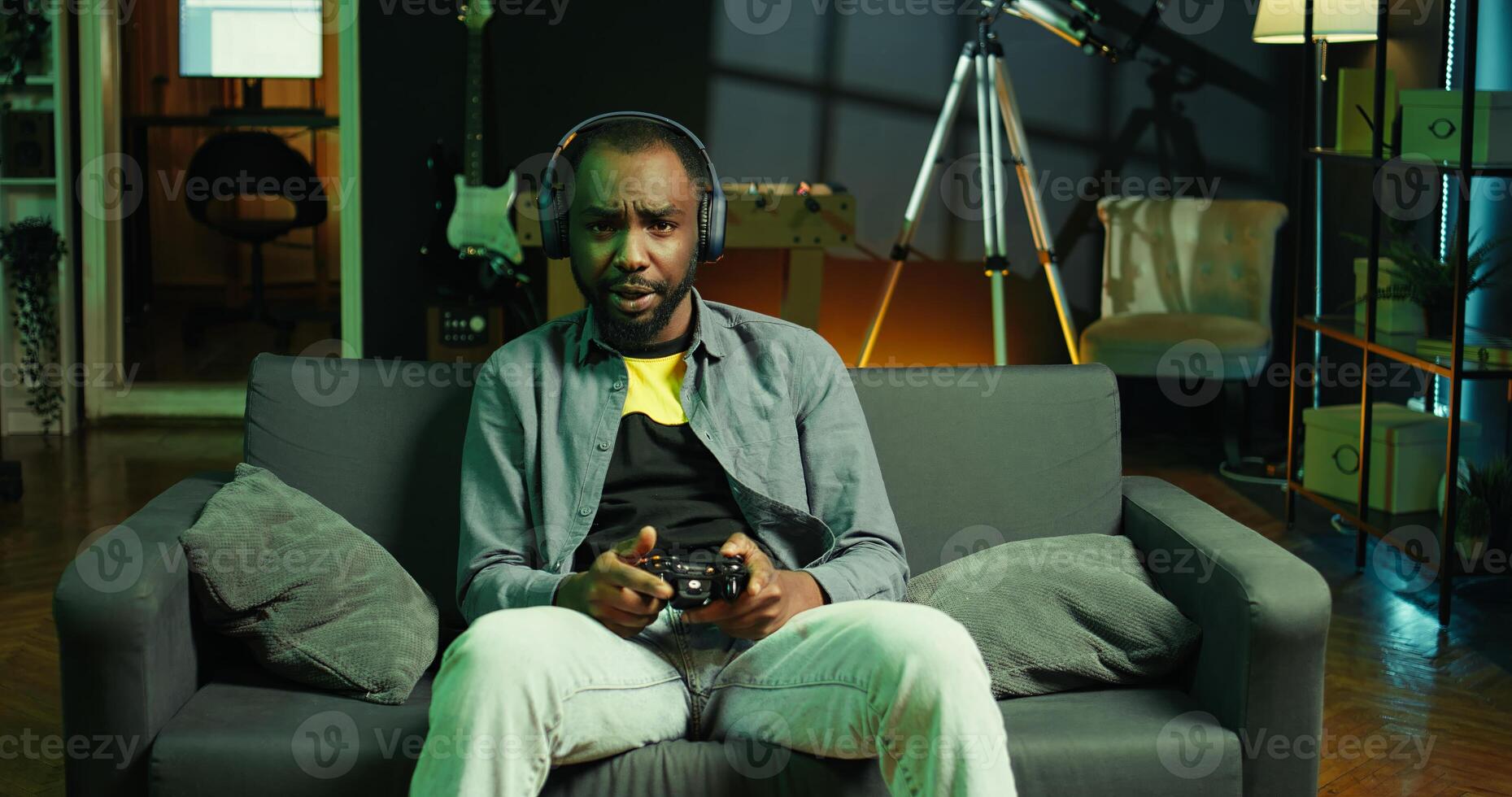 Gamer on couch using controller and headphones to play videogame at home, close up. Man in home theatre using high tech gaming console gamepad to defeat opponents in game, camera B photo