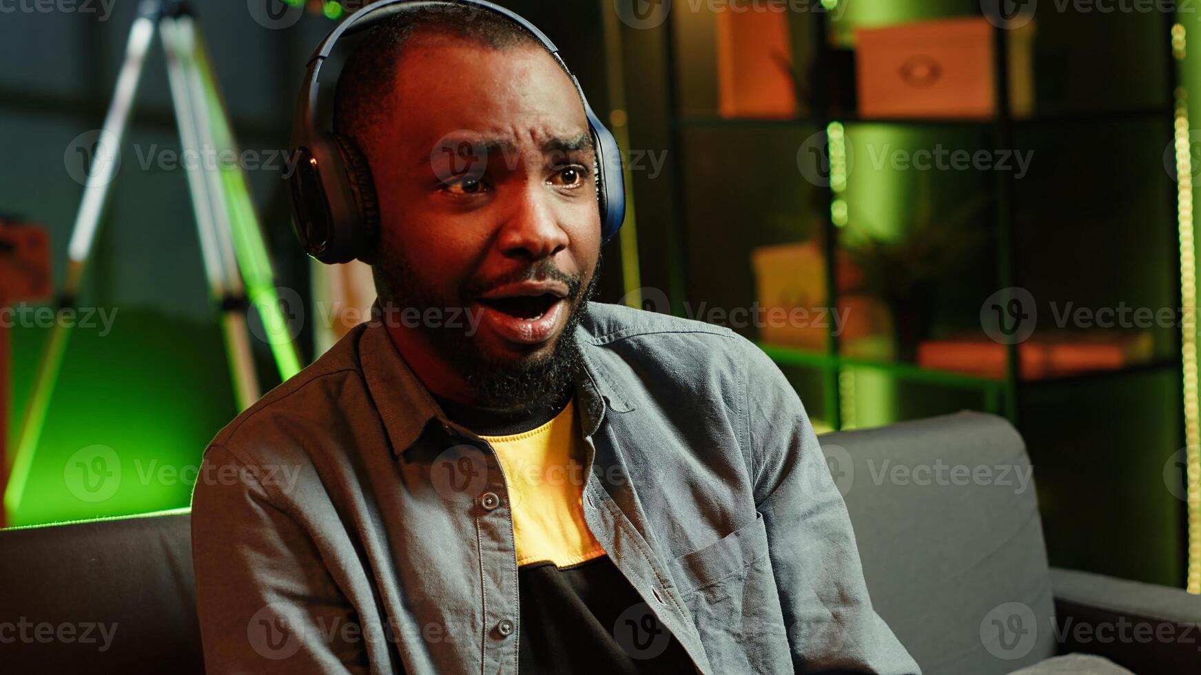 Gamer on couch using controller and headphones to play videogame at home, close up. Man in home theatre using high tech gaming console gamepad to defeat opponents in game, camera A photo