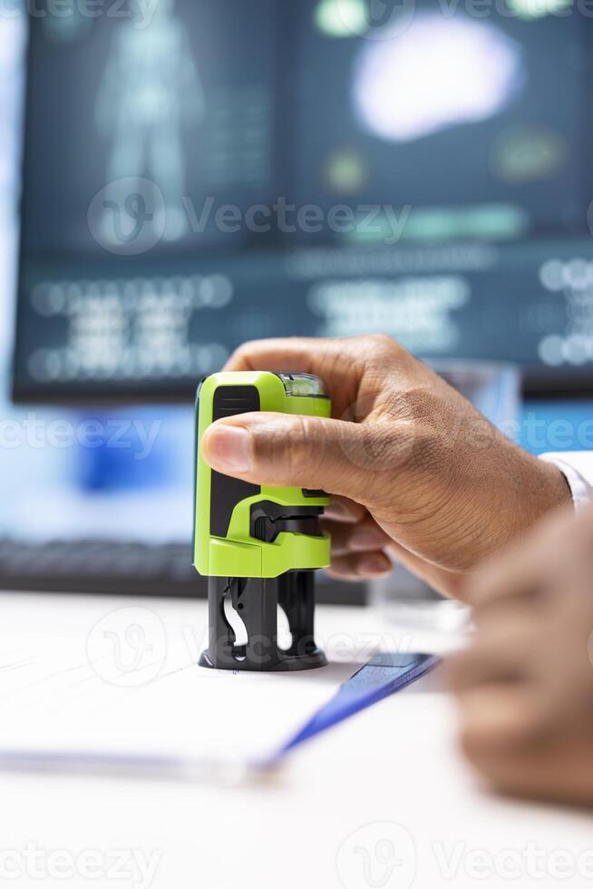 Specialist physician using his medical cabinet stamp to prescribe drugs and antibiotics for a patient, creating a prescription document to support recovery. Healthcare insurance. Close up. photo