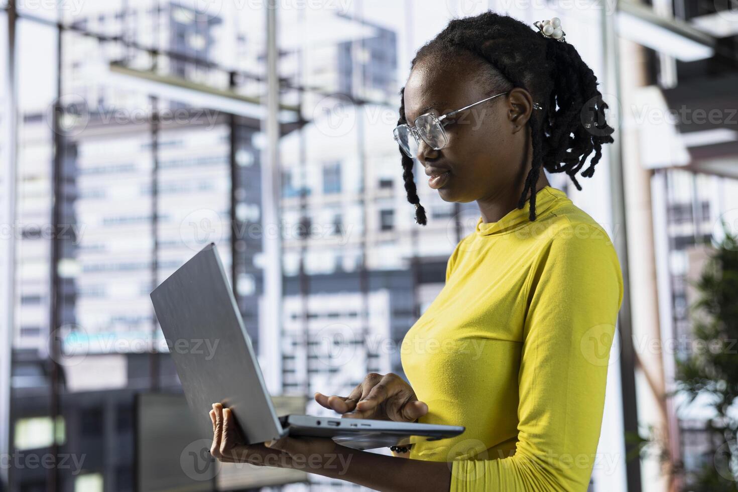 Worker standing in office using laptop during job shift, looking through online financial business documents. Company employee in workspace doing tasks on notebook, being productive photo