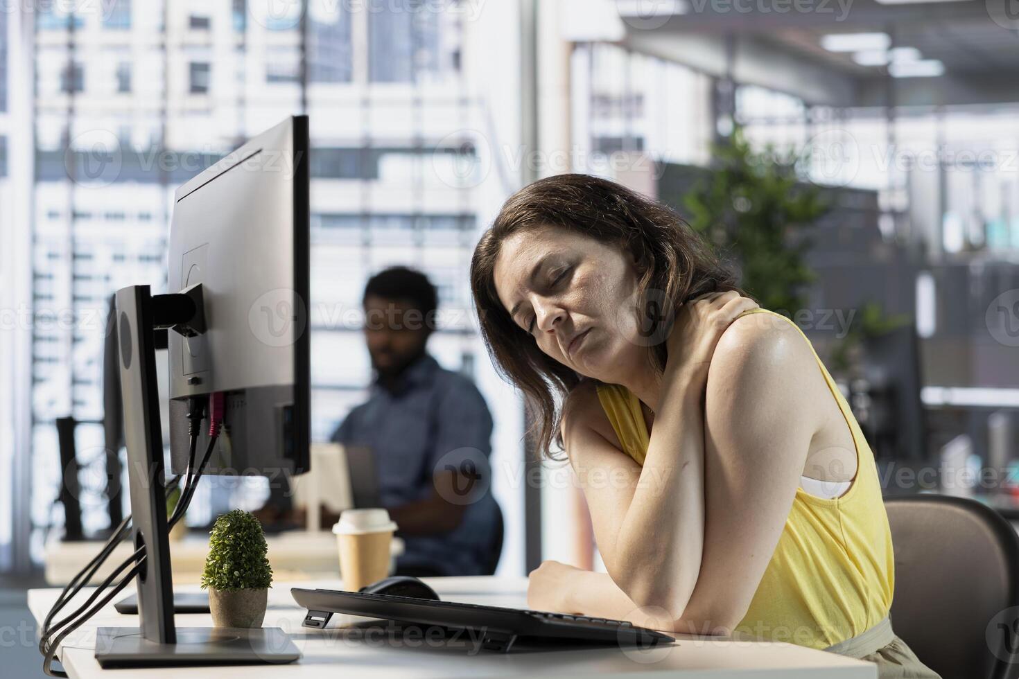 Worker in office feeling shoulder during job shift, feeling overworked while looking through online business documents. Fatigued company employee suffering injury in workspace while doing tasks photo