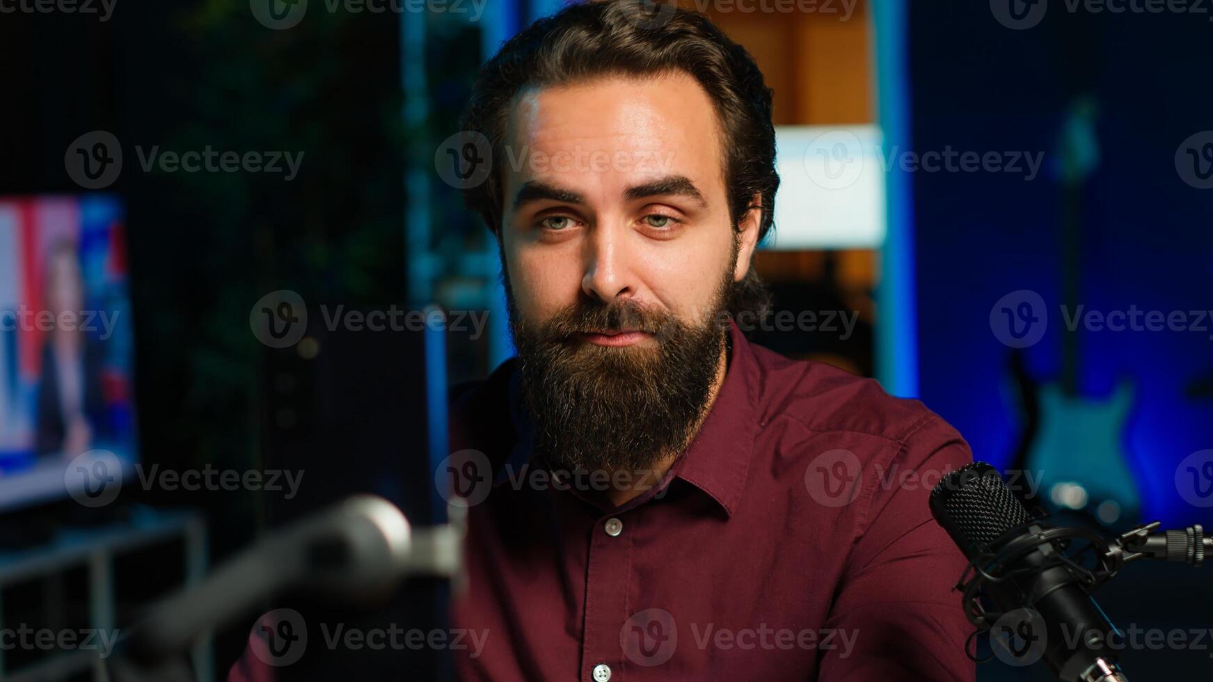 Happy influencer in home studio greeting audience, recording live broadcast using smartphone on selfie stick, close up. Man filming q and a session with mobile phone, answering questions, camera A photo