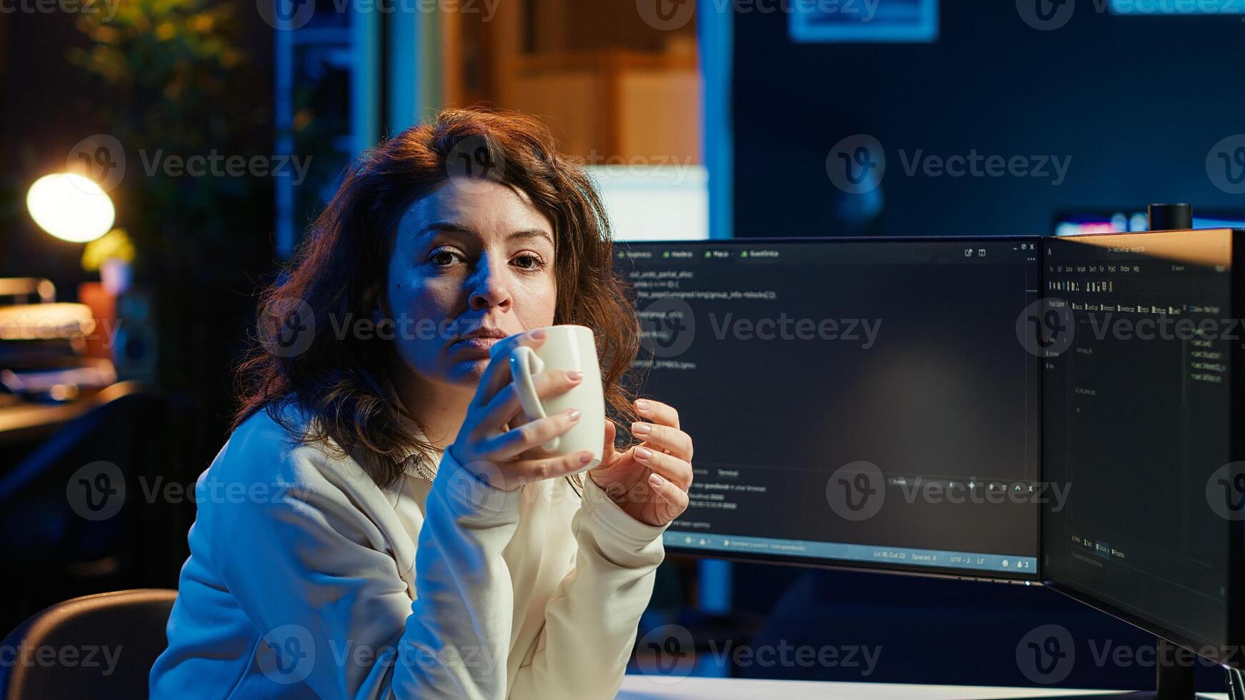 Portrait of smiling IT specialist drinking coffee while looking for company security vulnerabilities and preventing malware infections. Programmer enjoying hot beverage while writing code, camera A photo