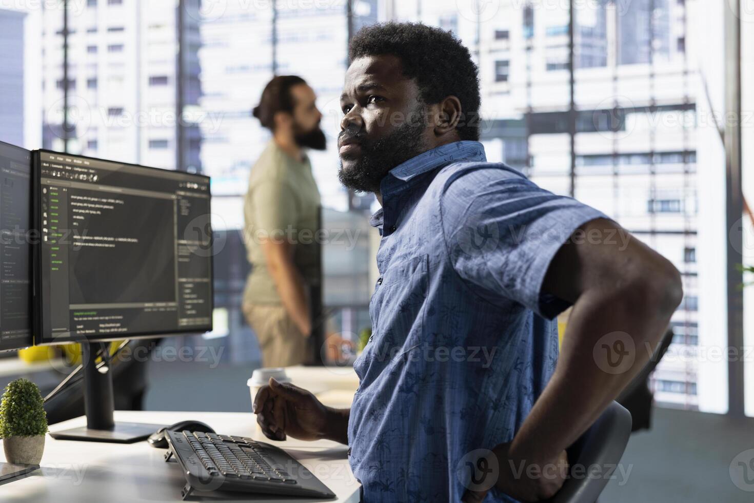 Worker stretching to relieve muscle strain while conducting code review to fix bugs, identifying technical issues with software. Man in office suffering back pain from bad posture, optimizing code photo