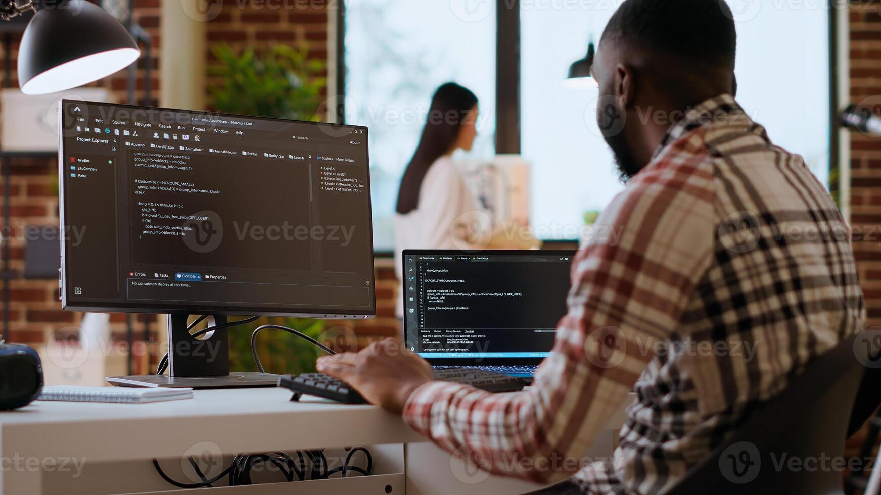 African american IT professional types programming code on dual monitors in home office, working on software development and internet security. Ideal setup for remote work and productivity. Camera B. photo