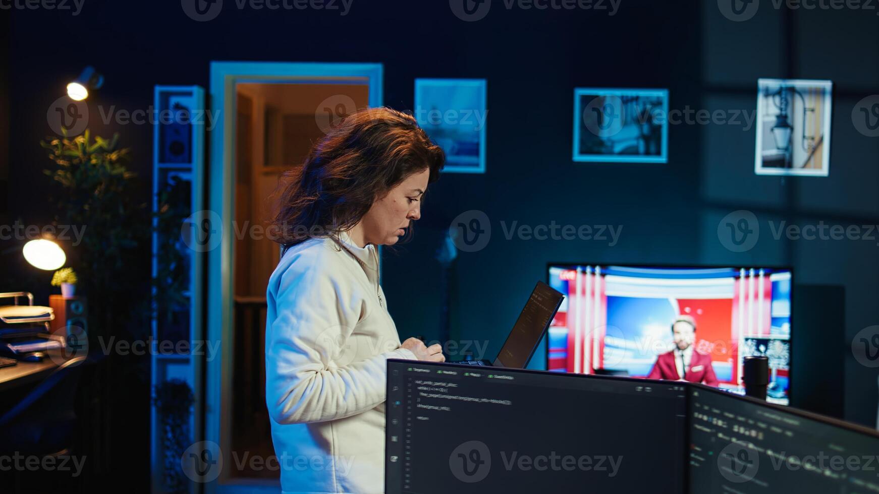 Woman walking in apartment designing and developing software applications using laptop. IT professional standing in living room, implementing and maintaining company systems, camera B photo