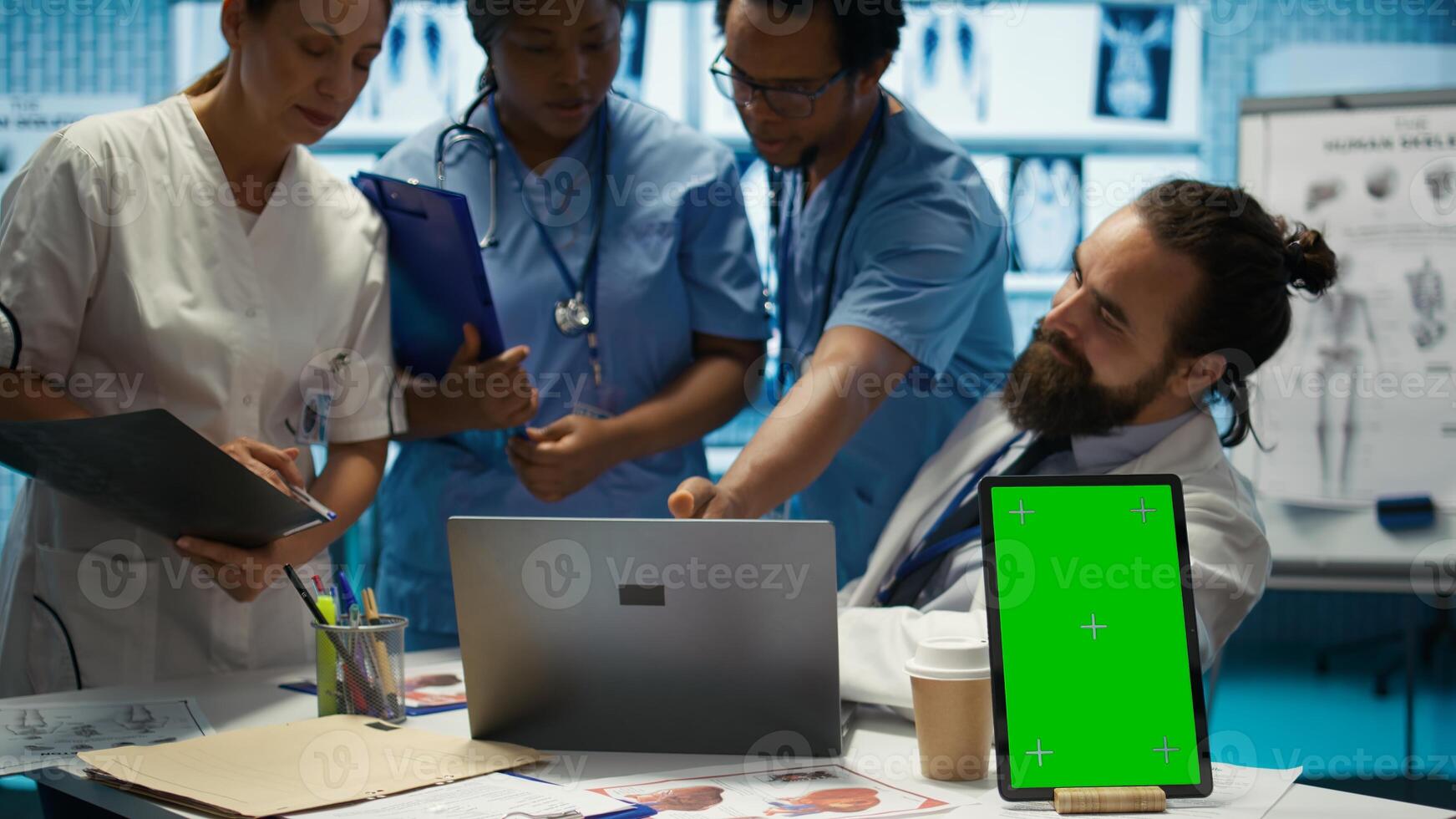 Team of doctors consulting analytics next to green screen on laptop in medical cabinet, examining x ray results to find the diagnosis. Licensed medics review hospital records at desk. Camera B. photo