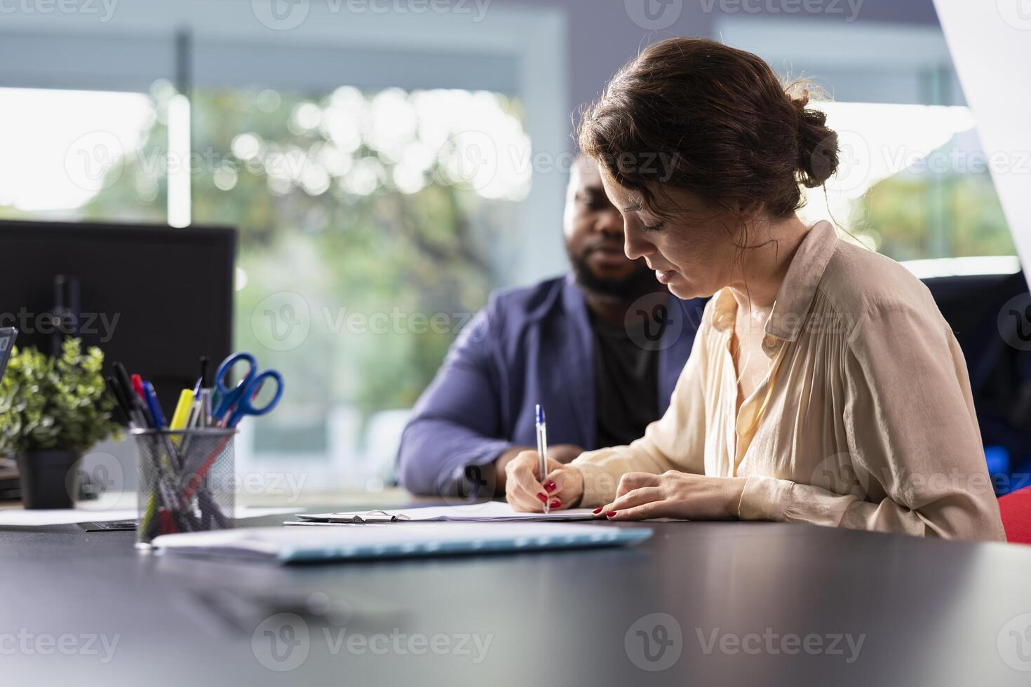 Woman in car dealership signing contract with salesperson after having concerns addressed, receiving compelling reasons for purchase. Client completing necessary sale paperwork for vehicle photo