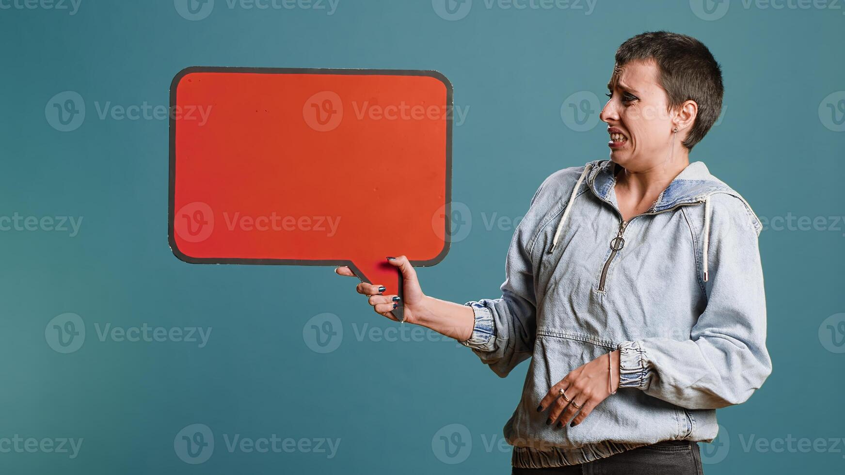Casual person presenting an empty speech bubble sign in studio, working on a commercial with billboard icon. Woman holding cardboard for advertisement against background. Camera B. photo