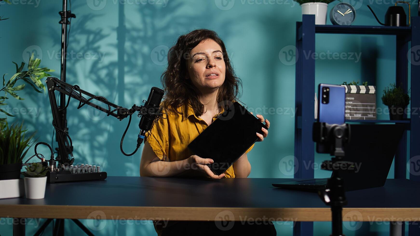 Tech expert presenting tablet in entry level low budget price range, filming from dimly lit home studio. Viral tech content creator reviewing digital device in front of online audience, camera B photo