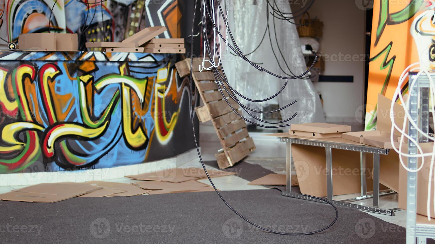 Jib down shot of spraying paint cans and pizza boxes left over in empty abandoned place with graffiti art on walls. Broken items in desolate location used as hanging place by teenagers photo