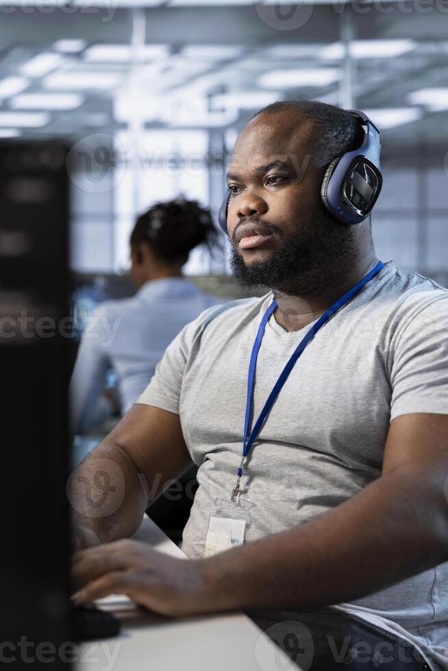 Technician listening music, using machine learning applications to optimize server farm operations. IT expert waring headphones hearing podcast while implementing server virtualization in data center photo