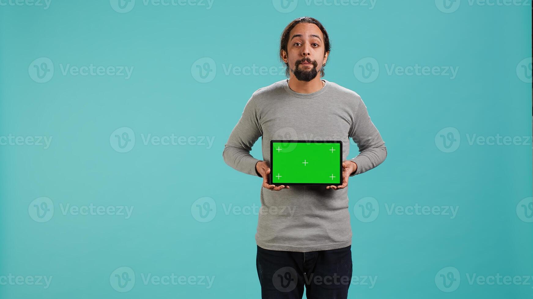 Influencer presenting green screen tablet, isolated over studio background. Arab person holding blank copy space chroma key device used for advertising brands, studio backdrop, camera A photo