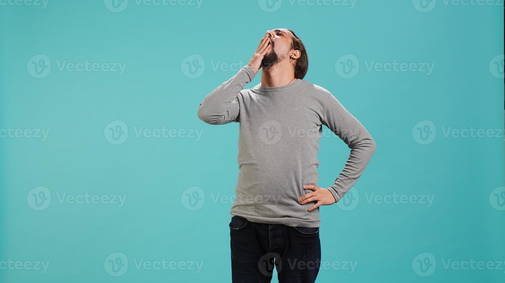 Man feeling exhausted and yawning, covering his mouth, isolated over studio background. Person being sleepy during morning, awaken too early, showing sleepiness, camera A photo