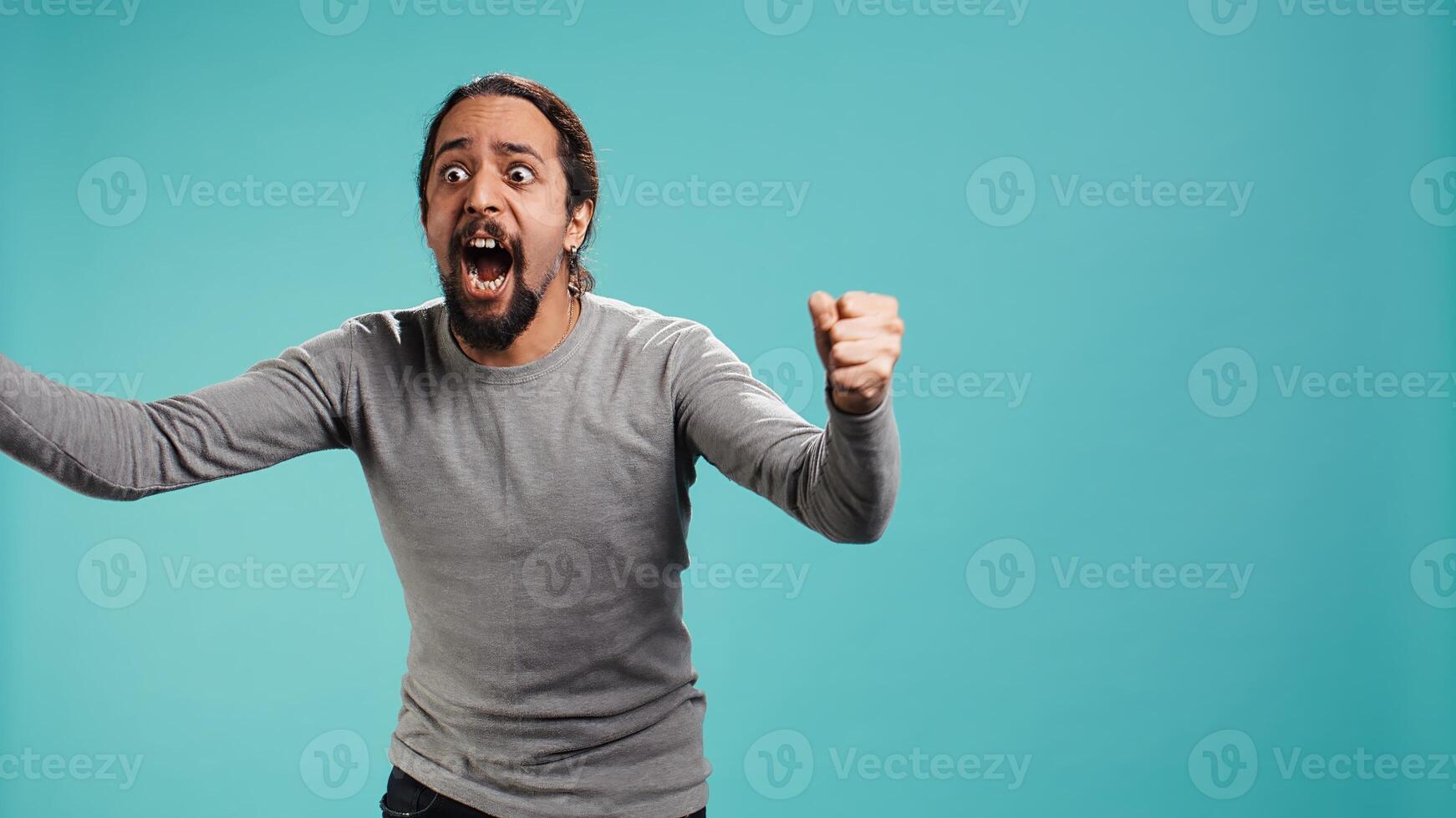 Portrait of irate man feeling outraged, yelling at friend, releasing pent up emotion, studio backdrop. Furious person full of rage screaming at mate isolated over blue studio background, camera B photo