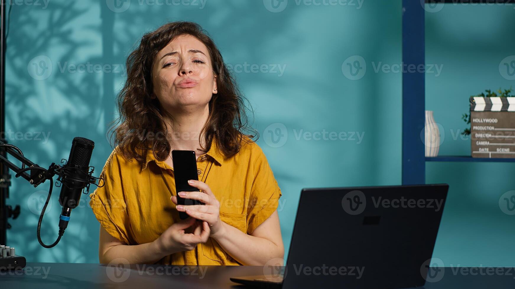 Cheerful entertainer presenting mobile phone from brand sponsoring , urging viewers to purchase it. Smiling woman does influencer marketing by advertising smartphone to audience, camera A photo