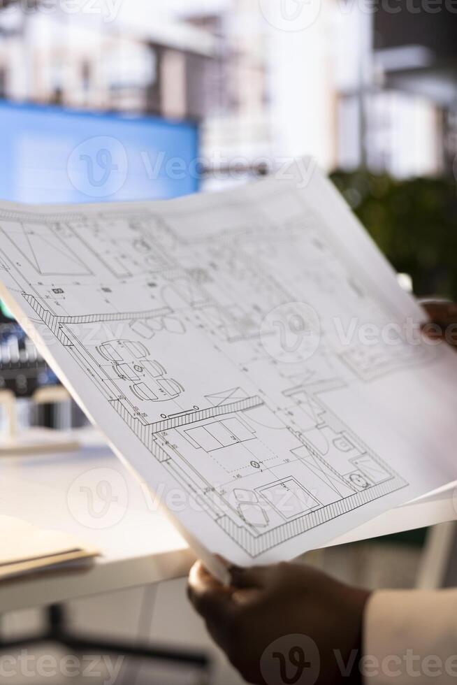 Architect looking at blueprint to scale of house room drawn in architectural engineering software. Close up of designer in office handling the planning and designing of building photo