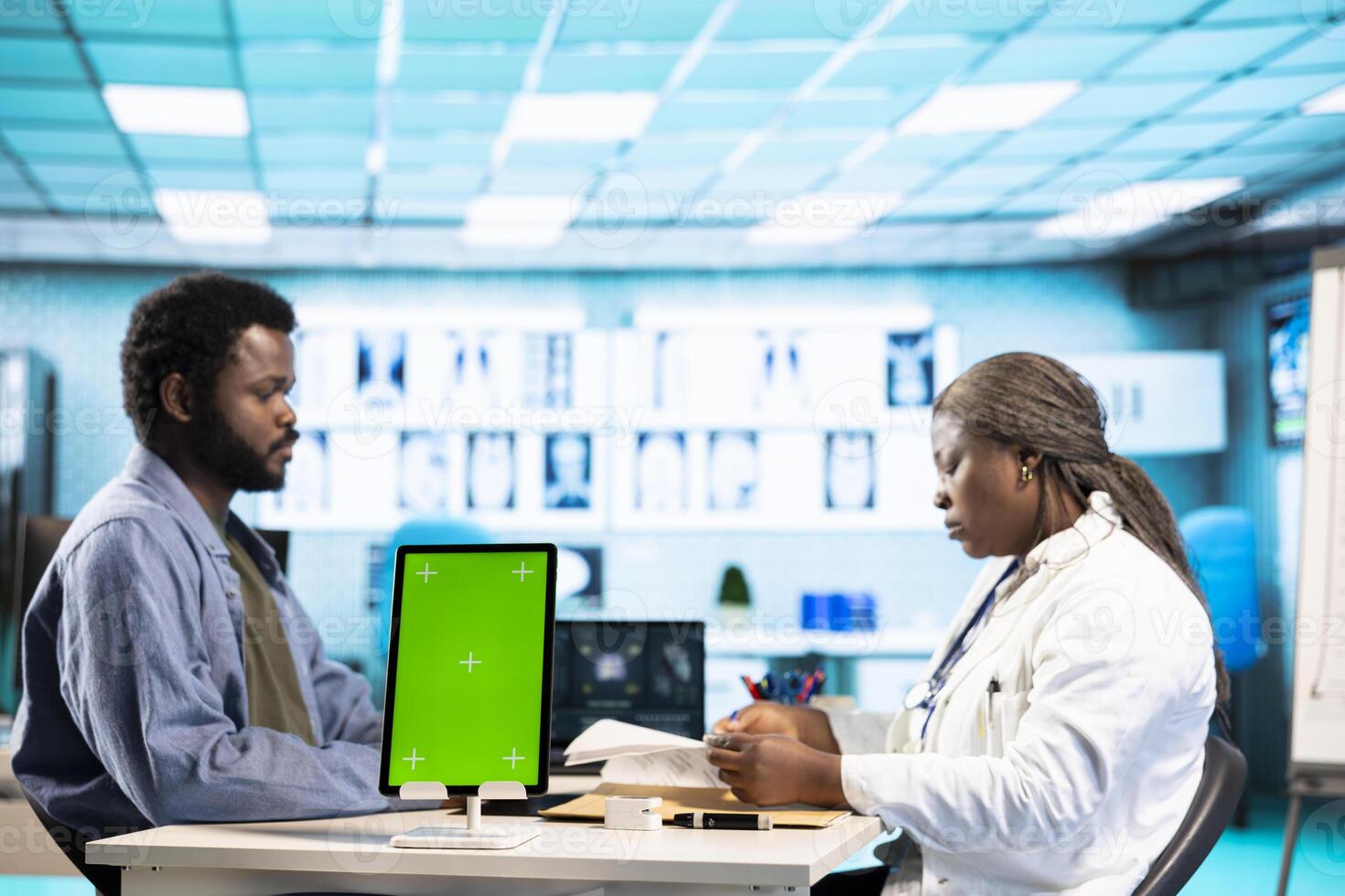 Black medic meets with patient next to isolated mockup display at the office, doing routine consultation and reviewing records for a treatment plan. Physician at private clinic. photo