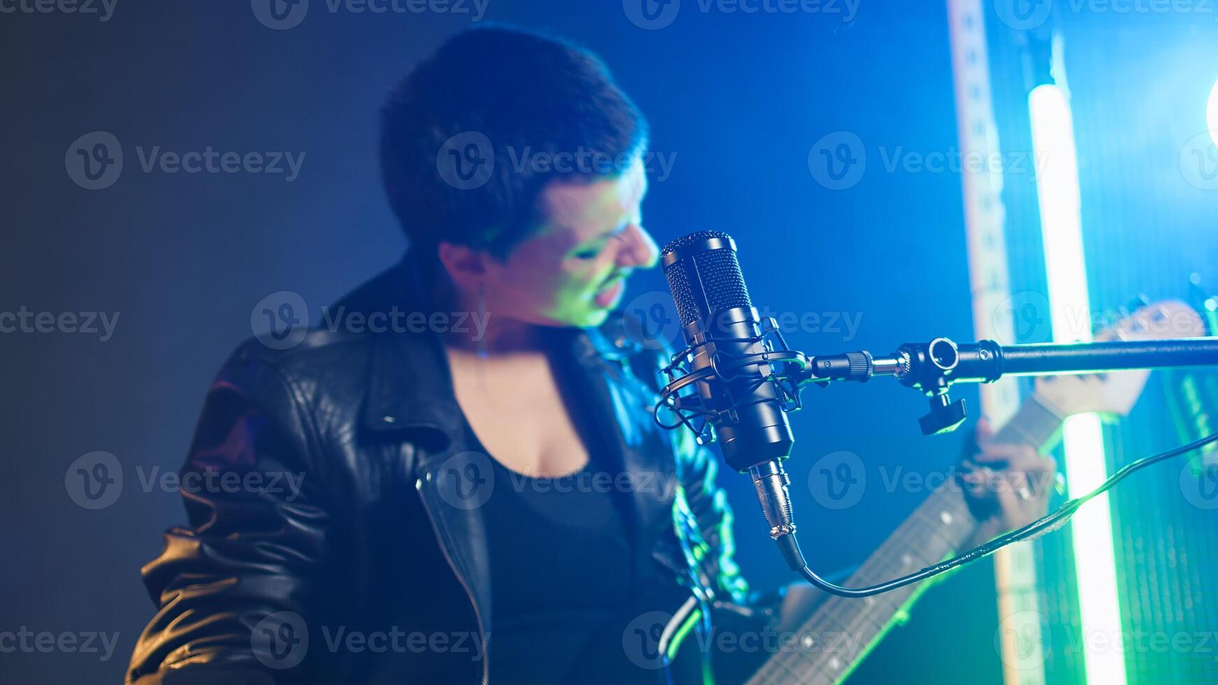Talented female musician playing guitar with confidence in a dark urban studio. Rebellious woman rocker with an edgy spirit and bold style creating a great fierce performance. Camera A. photo