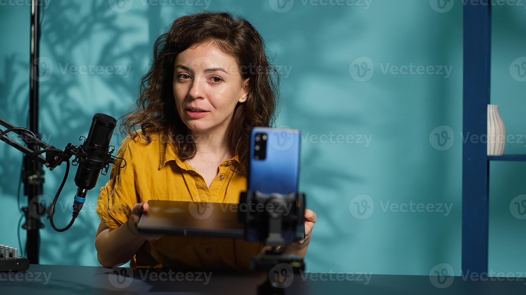 Internet show host using smartphone on phone holder, filming content about best gaming laptops. Media star recording notebook device review for interested viewers, camera A photo