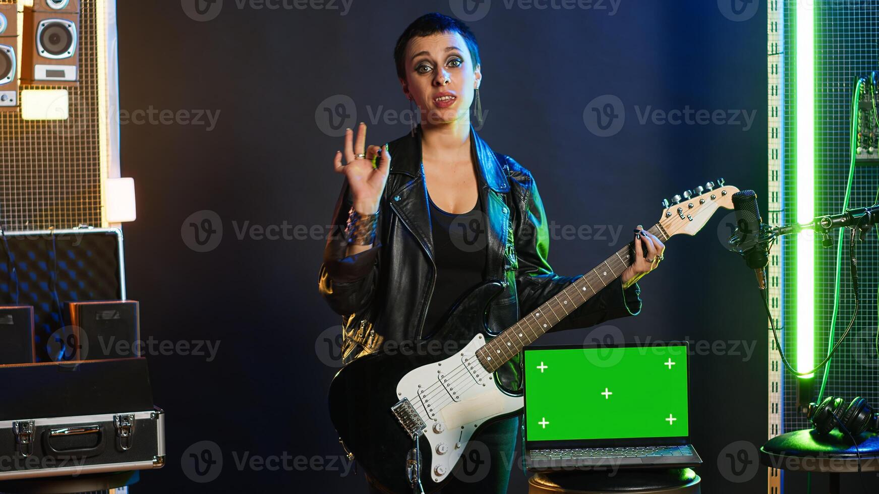 Cool rebellious rock star does a live performance next to chroma key screen at nightclub, feeling powerful in her leather jacket and dark make up. Trendy powerful singer performing. Camera A. photo