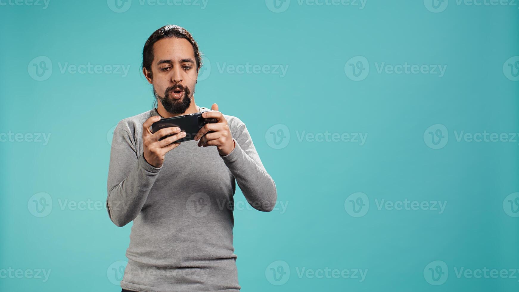 Man playing intense singleplayer videogames on smartphone, enjoying hobby. Gamer enjoying entertaining interactive game on phone, having fun, isolated over studio background, camera B photo