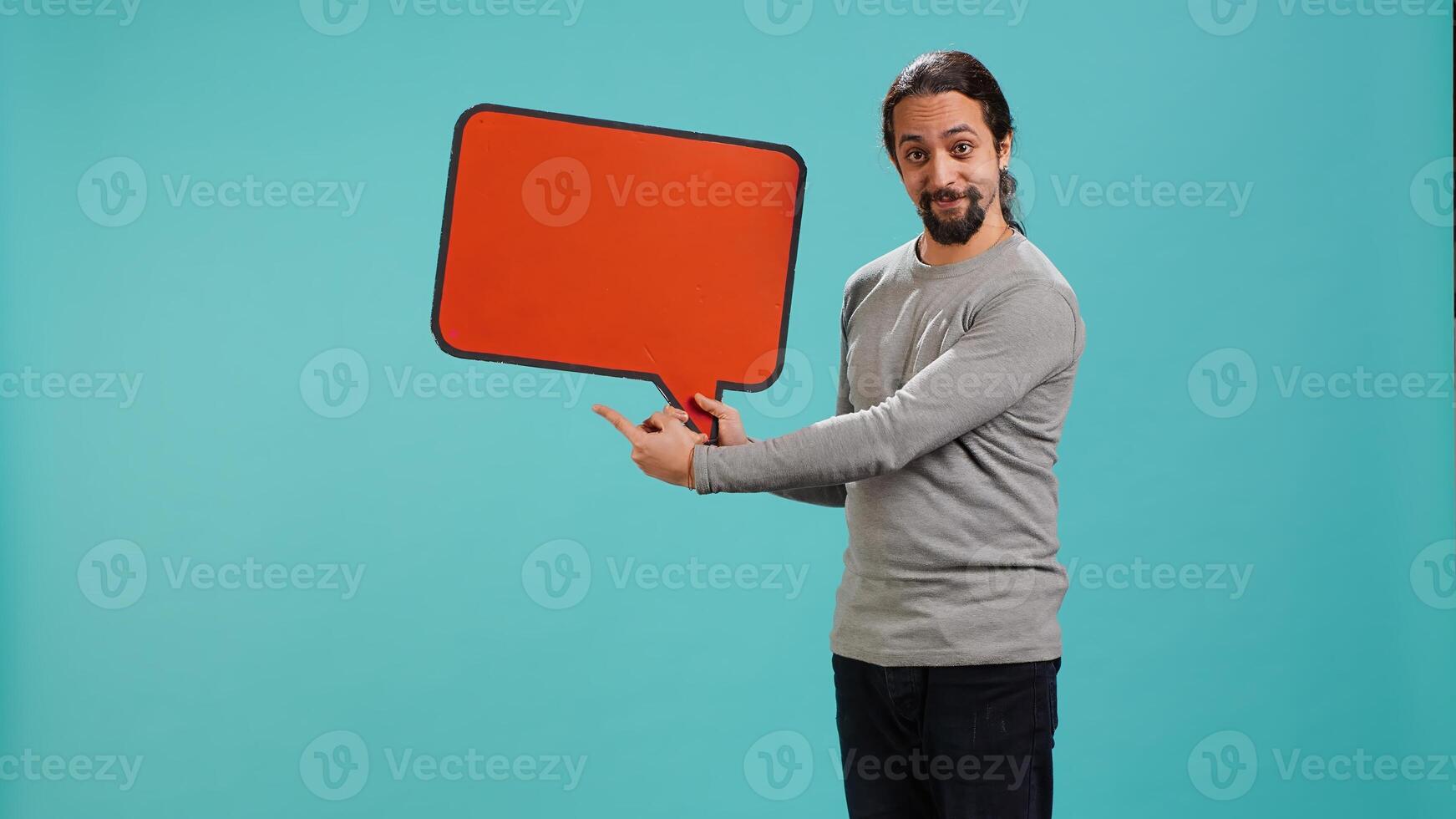 Smiling man holding red speech bubble sign of empty copy space for message. Joyous person presenting thought bubble cardboard used as promotion concept, studio background, camera A photo