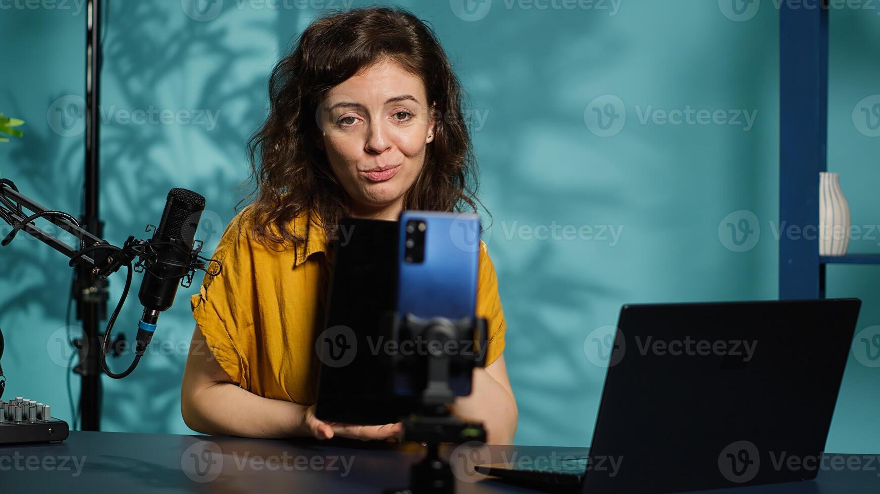 Tech expert presenting tablet in entry level low budget price range, filming from dimly lit home studio. Viral tech content creator reviewing digital device in front of online audience, camera A photo