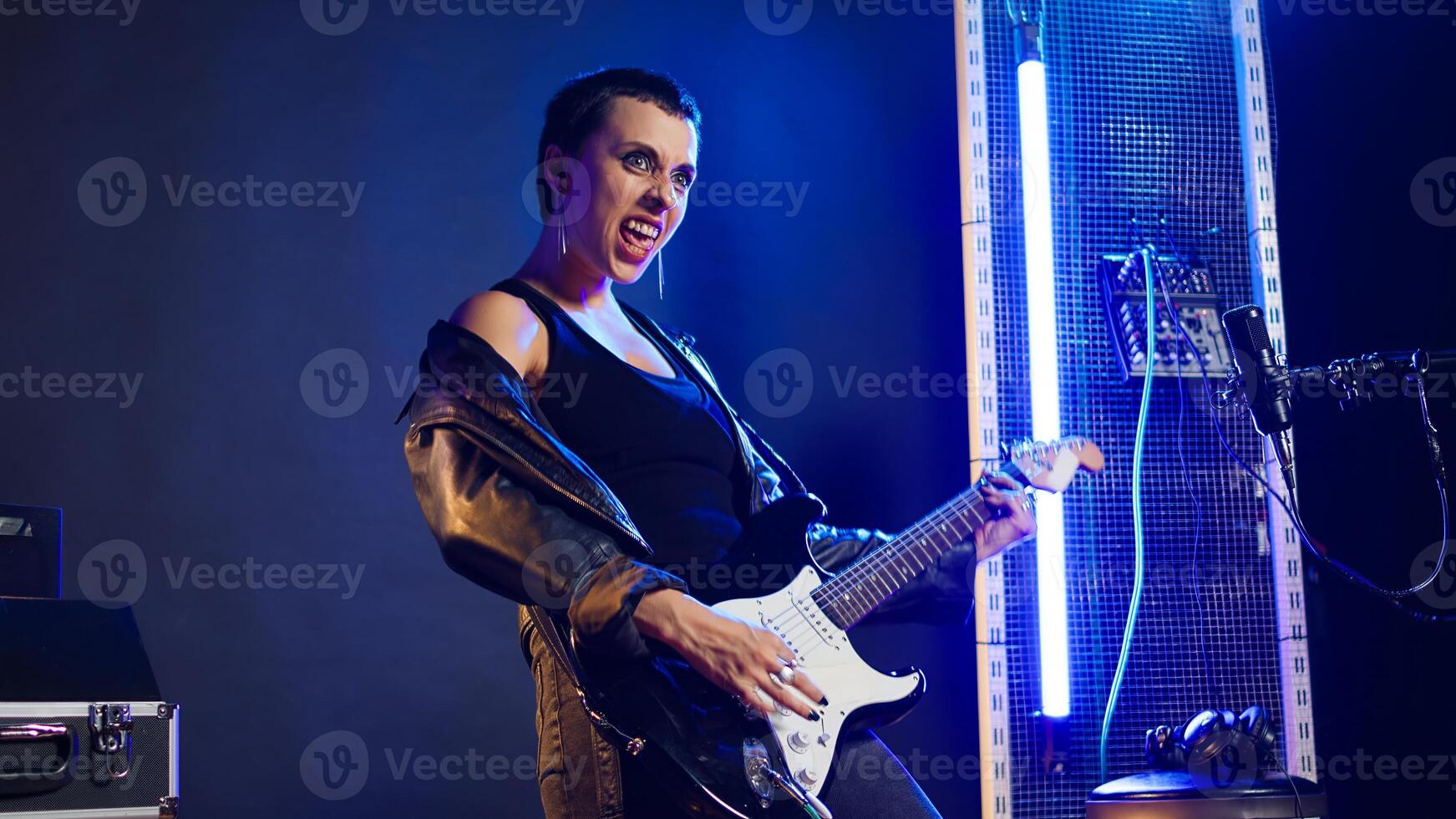Iconic edgy superstar sticking tongue out and playing guitar, creating a fierce powerful live performance. Crazy bold woman artist making silly faces, heavy metal music industry. Camera A. photo