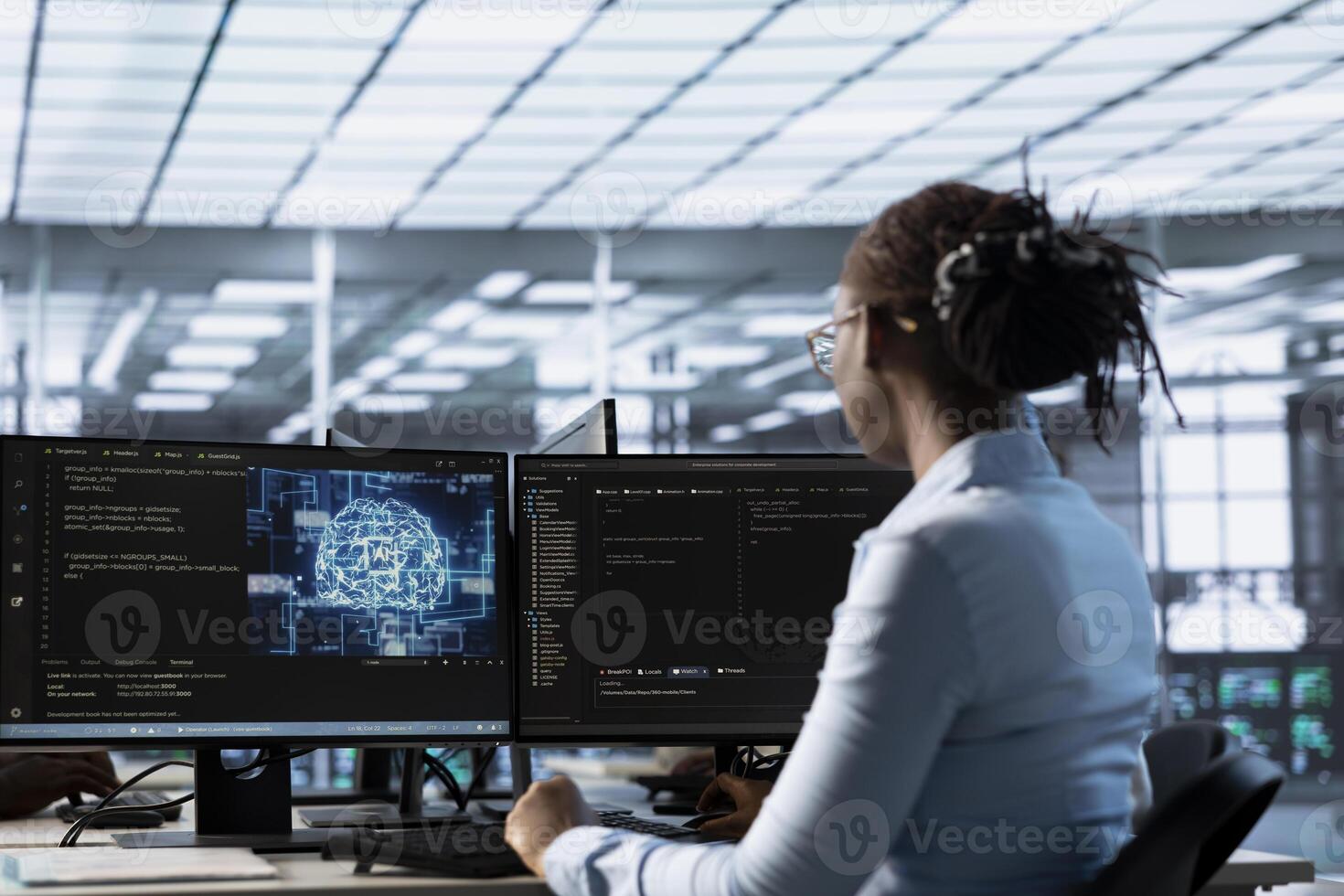 Engineer working at PC desk, doing checkup on AI server room providing computing resources. African american IT professional investigating data center mainframes using computer photo