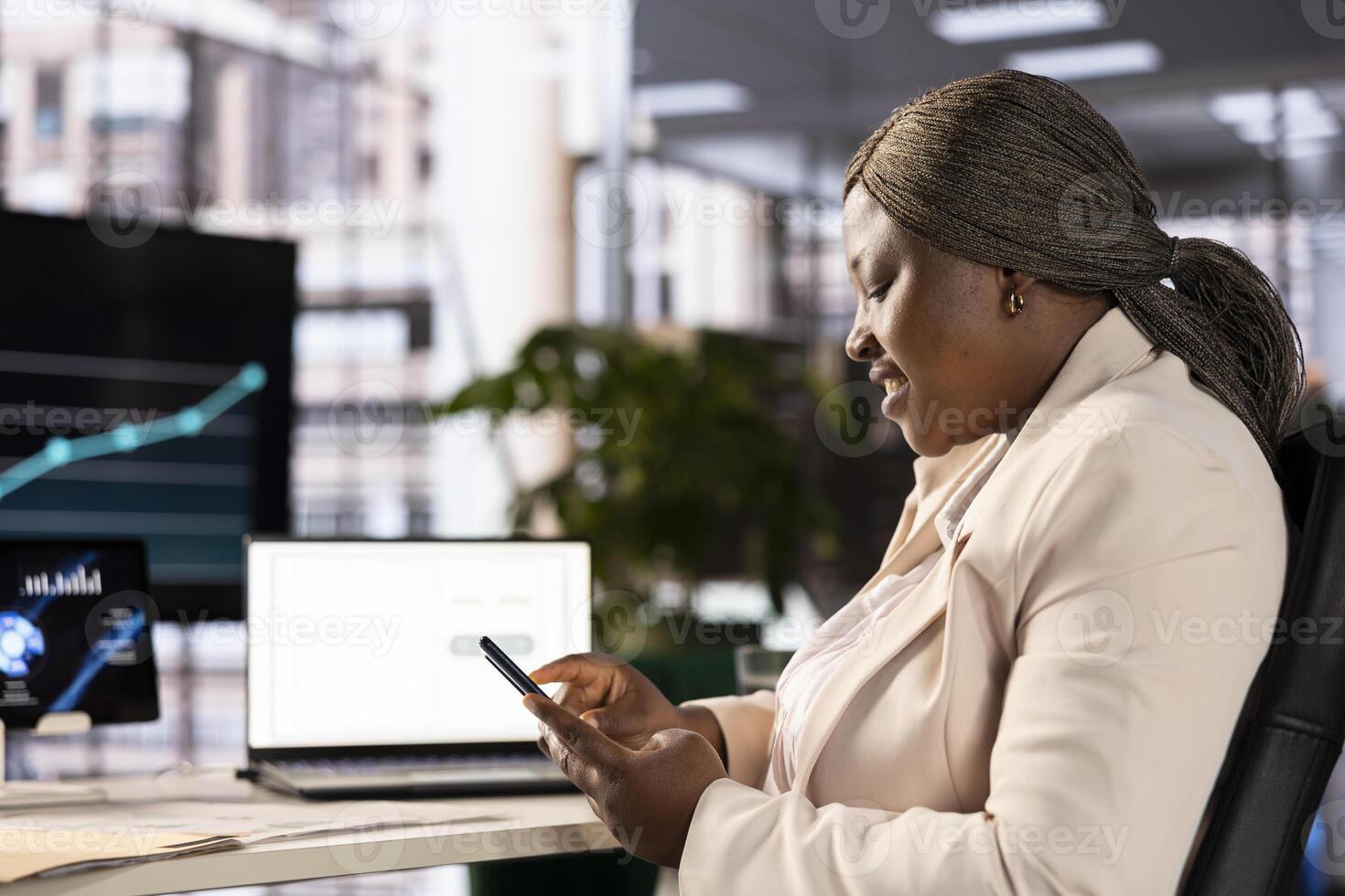Smiling employee taking break from doing research in office to increase company agency profit. Jolly businesswoman texting stakeholders, talking about new investment project photo